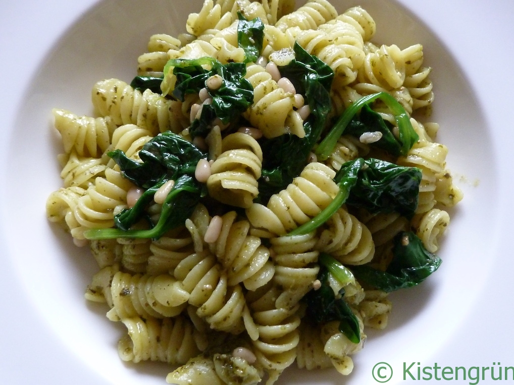 Pesto-Pasta mit blanciertem Spinat und Pinienkernen in einem weißen Teller