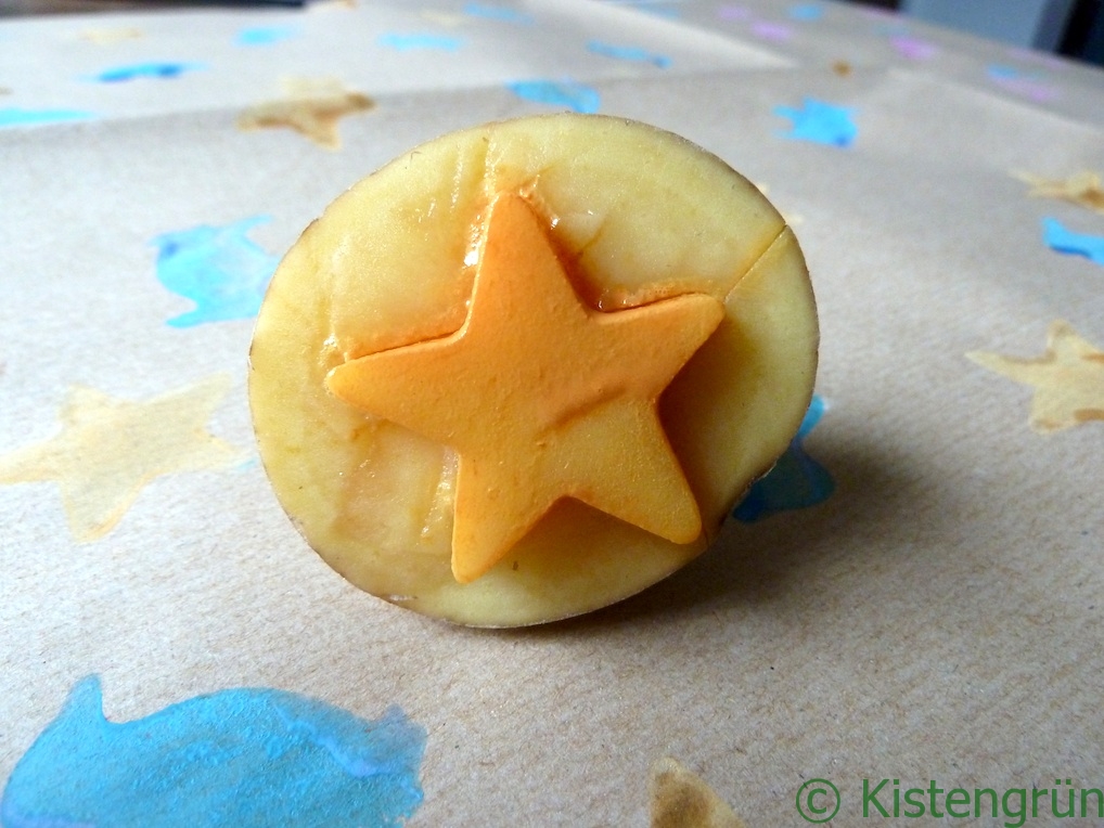 Eine Kartoffelstempel mit einem orangenen Stern auf einem Bogen selbst gestaltetem Geschenkpapier