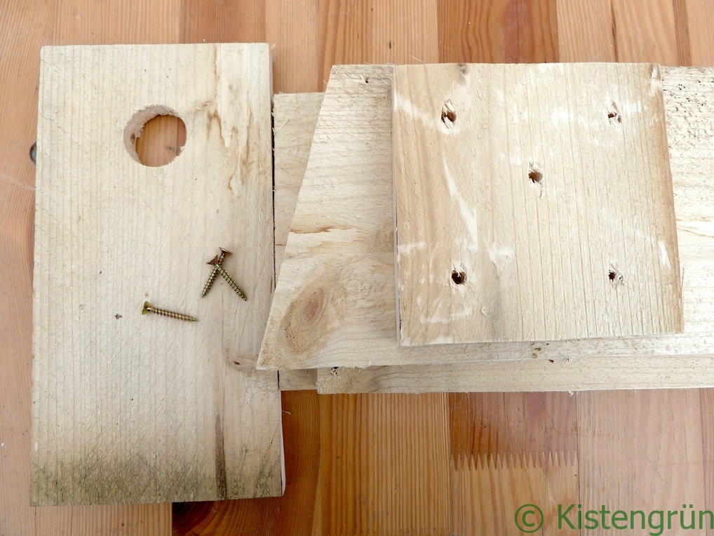 Bausatz für einen Nistkasten: eine paar Bretter und Schrauben auf einem Holztisch.